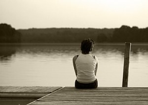 Photo of a man sitting, idling his time, on the dock of the bay.